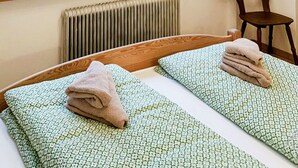 Hotellihuone, jossa on kaksi sänkyä, näköala vuoristomaisemaan, puinen tuoli ja patteri.