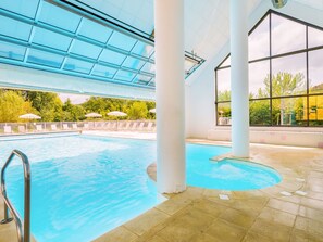 An indoor swimming pool with clear glass ceilings, white columns, and a view of greenery outside.