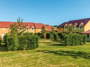 A row of yellow buildings with red roofs, surrounded by green hedges and grass.