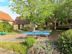 An outdoor ping pong table set up in a garden with stone buildings in the background.