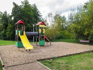 Ein Spielplatz mit einer gelben Rutsche und zwei Klettergerüsten, umgeben von Kiesflächen und Grünanlagen.