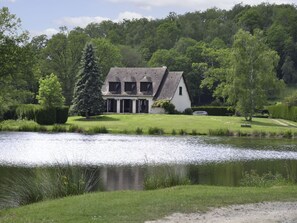 Ein zweigeschossiges Haus mit geneigtem Dach, umgeben von einem gepflegten Rasen und einem Gewässer.