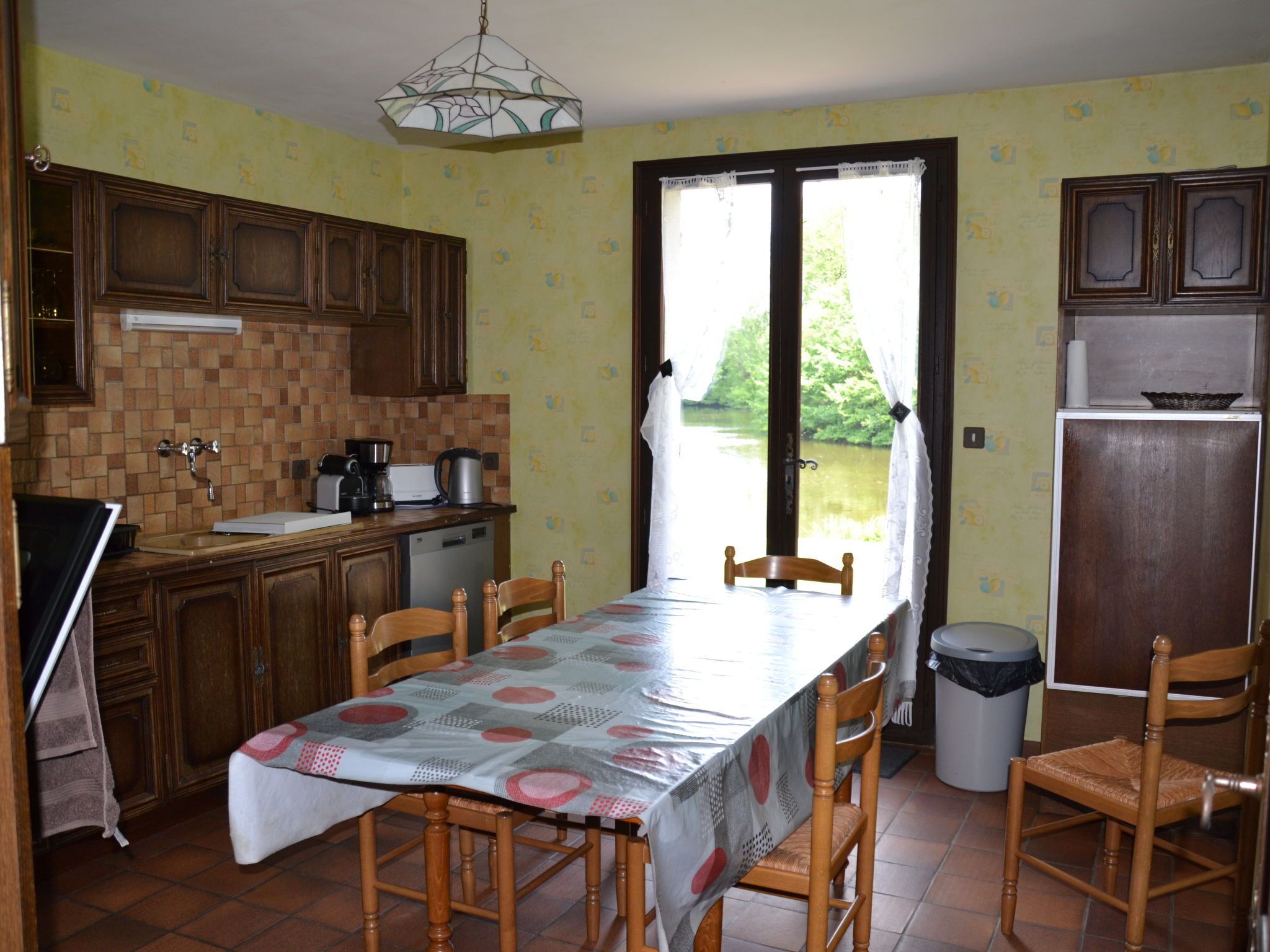 A kitchen with wooden cabinets, a dining table with chairs, a sink, and a window with curtains.