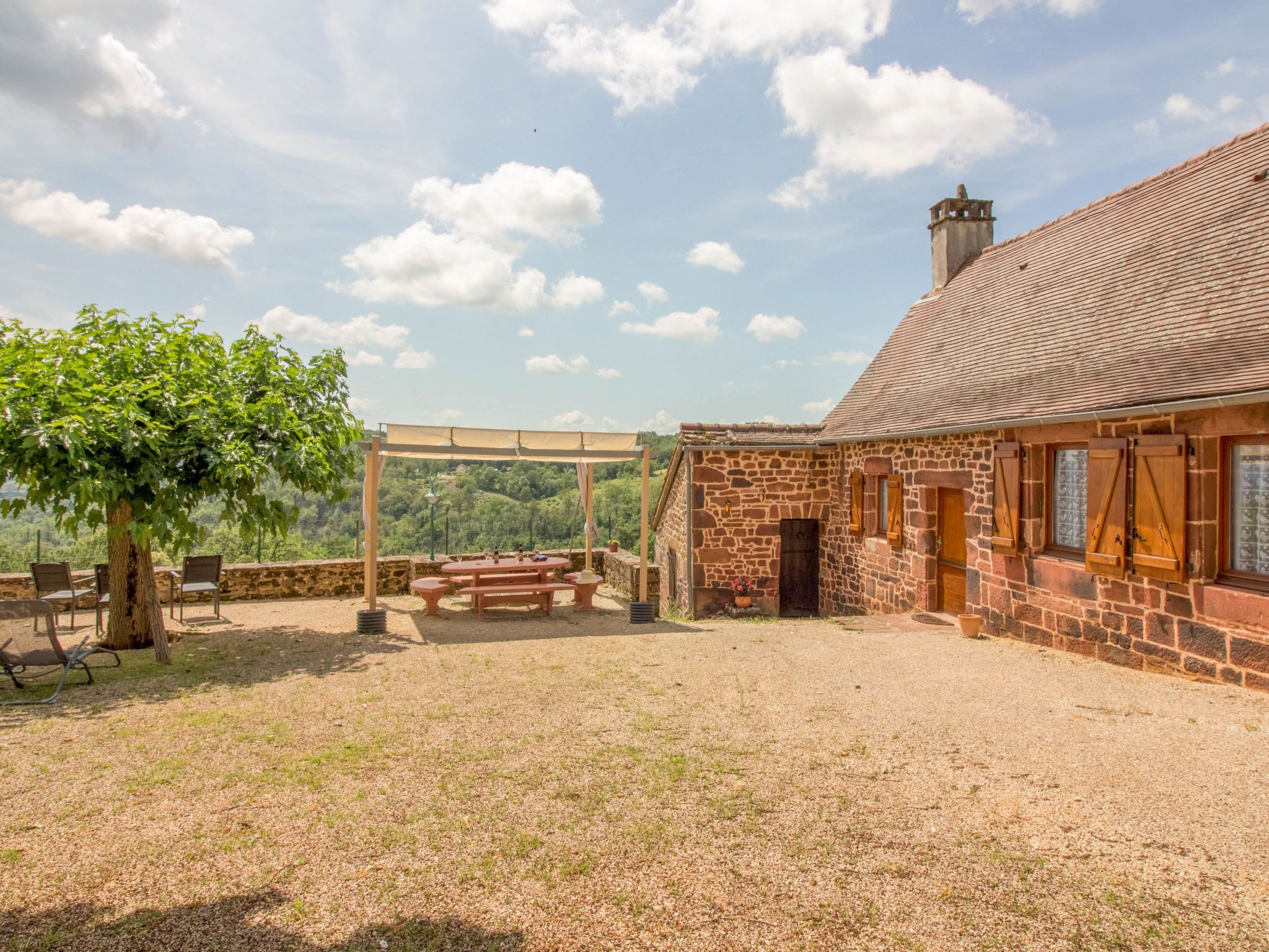 Ein Steinhaus mit Ziegeldach, einer Pergola und einem Picknicktisch auf einer Wiese.