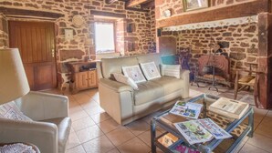 A rustic living room with stone walls, a wooden ceiling, a sofa, a glass coffee table with magazines, and a fireplace.
