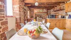 A rustic dining area with a stone wall, wooden ceiling, and a long table set for a meal.