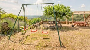 A patio with a swing set, picnic tables, and a view of the countryside.