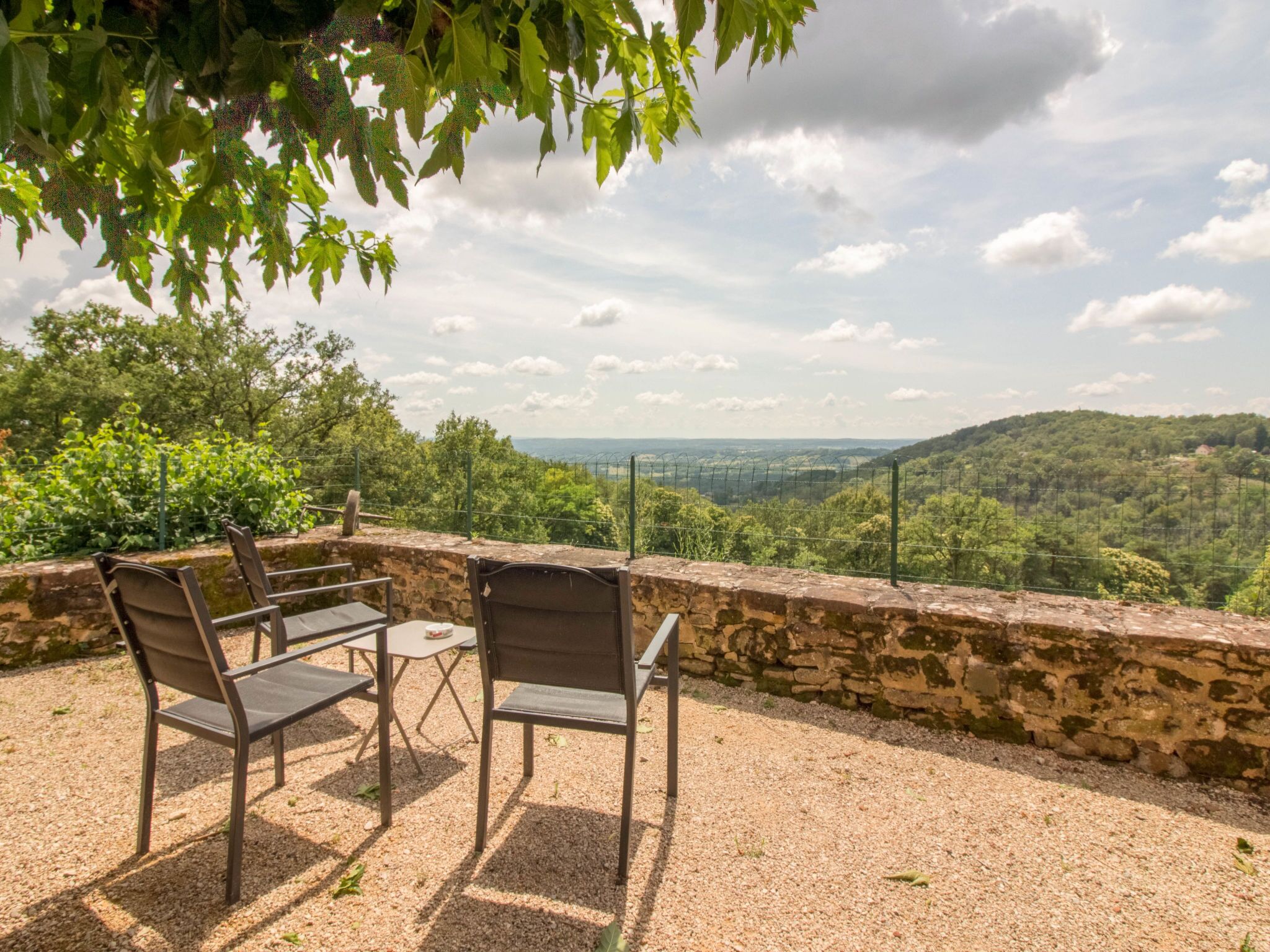 Un patio con dos sillas y una mesa, con vistas a un paisaje pintoresco con colinas y un cielo despejado.