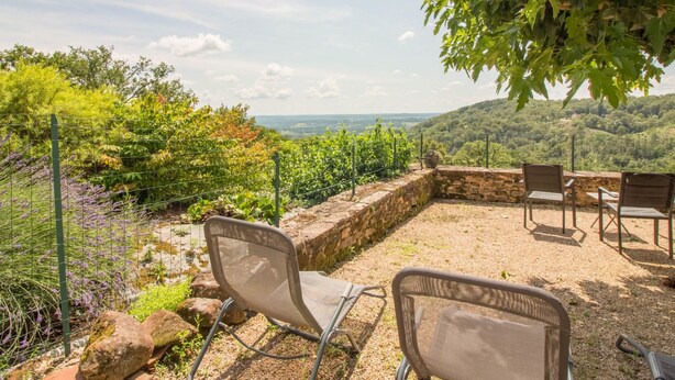 A patio with outdoor seating and a view of a vineyard and hills.
