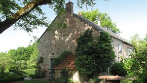 A stone building with a sloped roof, surrounded by lush greenery and a well-maintained garden.