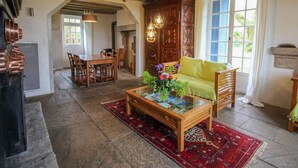A spacious living area with a wooden coffee table, a sofa, and a dining table with chairs. There is a large window providing natural light and a view of the outdoors.