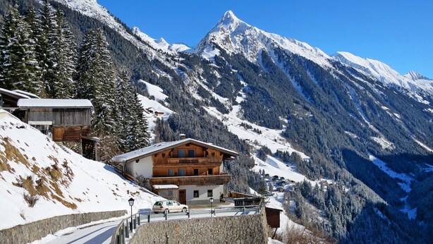 A mountain lodge with a wooden exterior, a stone retaining wall, and a snow-covered landscape with pine trees. - Hochwart by Interhome (Mayrhofen)
