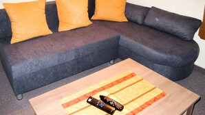 A sectional sofa with three orange cushions and a wooden coffee table with two remote controls. - Hochwart by Interhome (Mayrhofen)