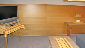 A room with a wooden floor, a television on a stand, a small table with a tablecloth, and a wooden cabinet. - Hochwart by Interhome (Mayrhofen)