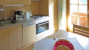 Een keuken met houten kastjes, een fornuis, een oven, een koffiezetapparaat en een raam met gordijnen.