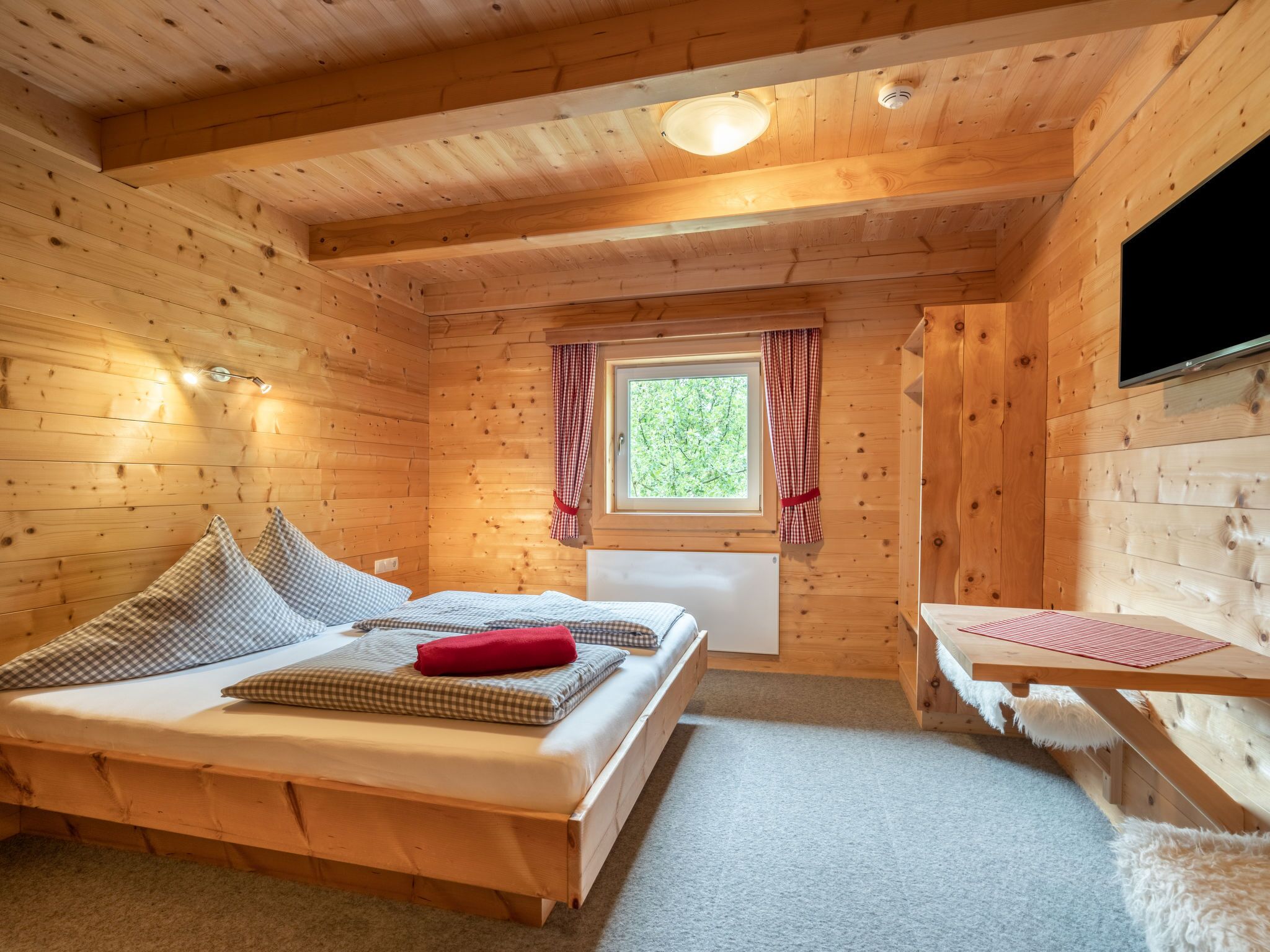 Una habitación cálida de cabaña de madera con una cama, una mesita y una ventana con cortinas.