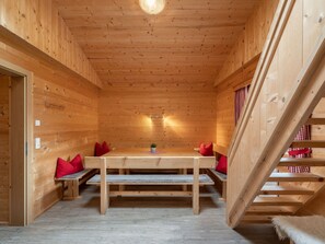 A wooden interior with a dining table, benches, and a staircase.