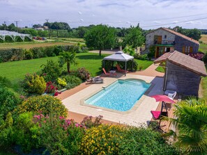 Ein Schwimmbecken mit Sonnenschutz, umgeben von einem Garten mit verschiedenen Pflanzen und Blumen.