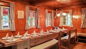 A wooden dining area with long tables set for a meal, benches, and a crucifix on the wall.
