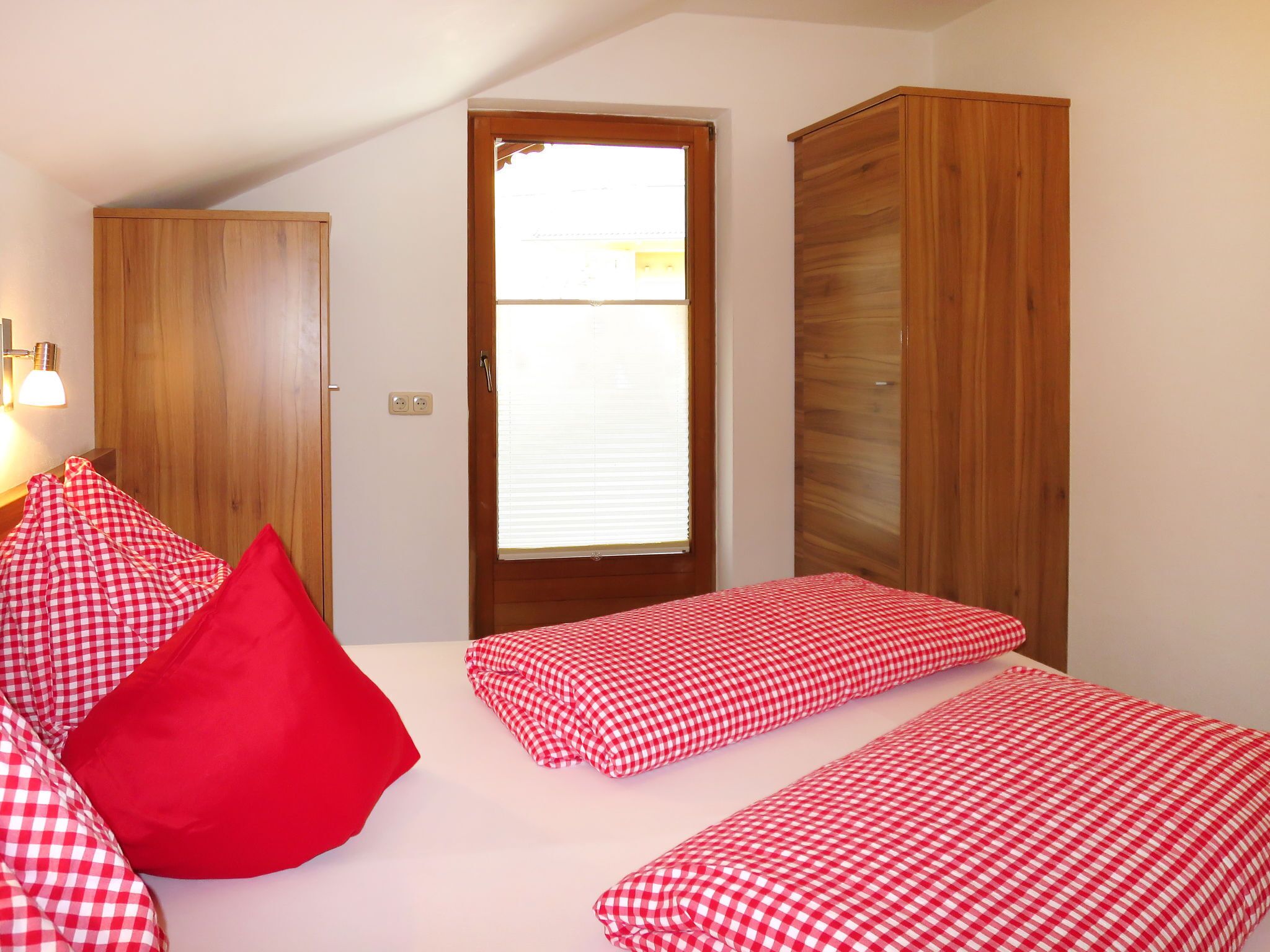 A bedroom with a bed, two pillows, a wardrobe, and a door with blinds.