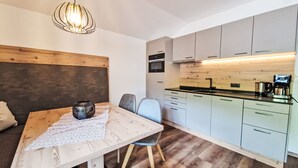 Een moderne keuken met lichte kasten, een houten eettafel met een kantoneet en een hangende hanglamp.