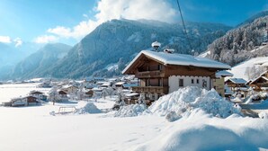 Een besneeuwd dorpje met traditionele houten huizen, een opvallend gebouw met een balkon, en bergen op de achtergrond.