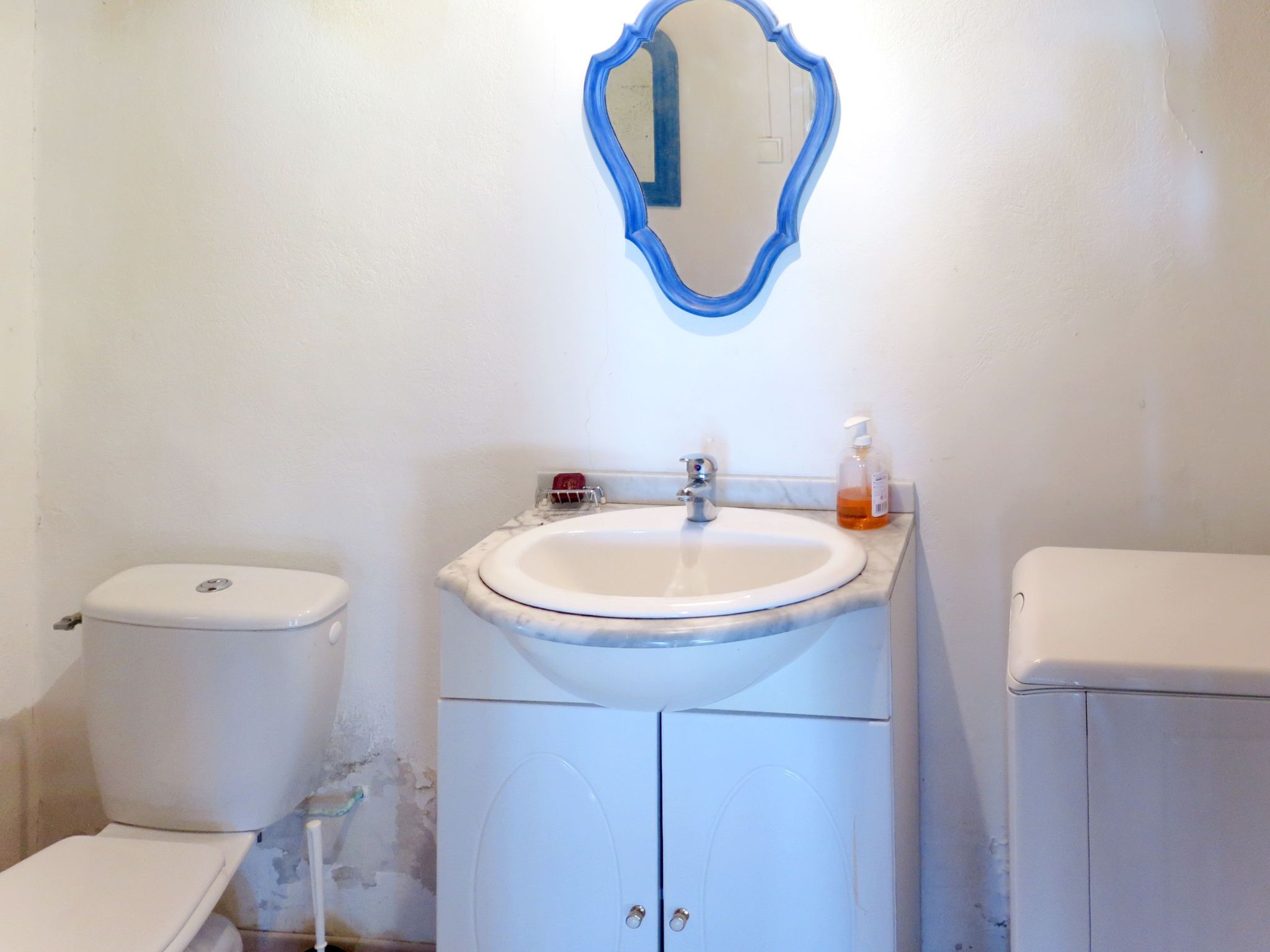 A bathroom with a white toilet, a sink with a mirror above it, and a soap dispenser on the sink.