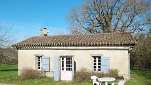 A small, single-story building with a tiled roof, a door, and two windows with shutters. There is a table and two chairs outside. - Marquefabe by Interhome (Labretonie)