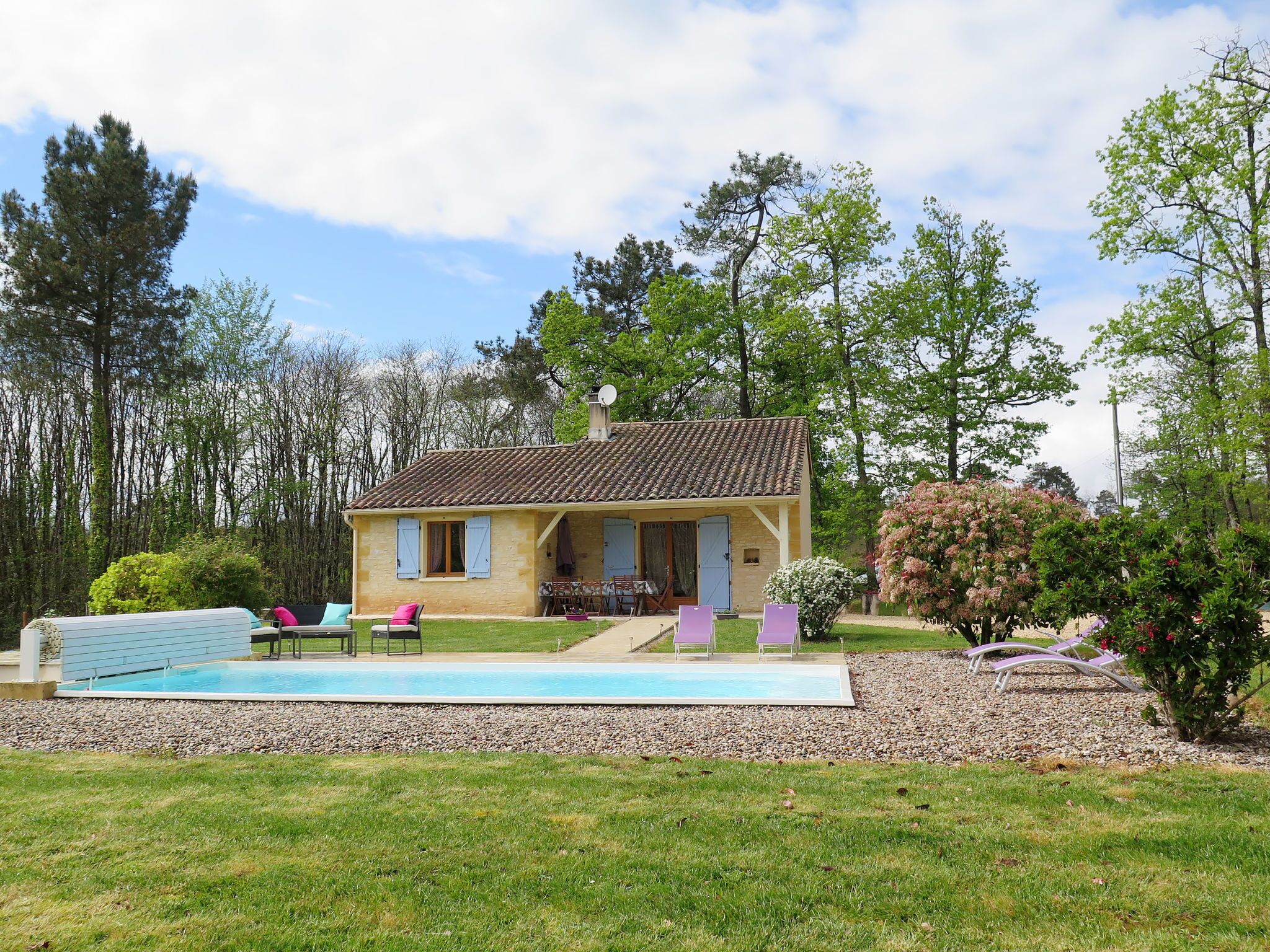 Une maison à deux étages avec une piscine, entourée d’arbres et d’un jardin.
