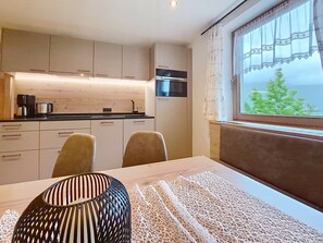 A modern kitchen with a dining area, a window with a view, and a table with a decorative vase. - Apartment Neuner by Interhome (Mayrhofen)