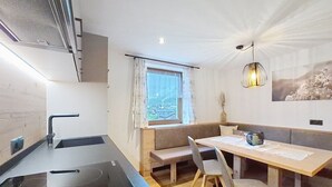 Eine moderne Küche mit einem schwarzen Herd, einer Spüle und einem Fenster mit Vorhängen. Es gibt einen Holzessttisch mit Stühlen und einer Bank.