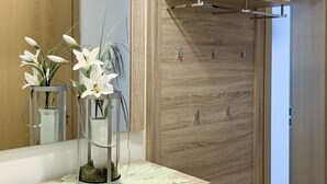 Ein modernes Zimmer mit einem Holzschrank, einem Schminktisch mit Spiegel und einer dekorativen Vase mit weißen Blumen.