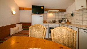 Una cucina funzionale con zona pranzo, che comprende un tavolo di legno, sedie in vimini, un televisore, un frigorifero e un piano cottura.