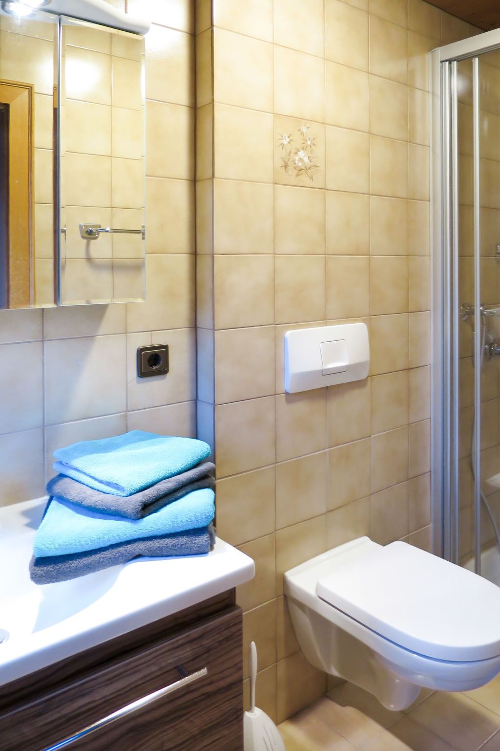 Un baño con inodoro, lavamanos y espejo. Hay toallas apiladas sobre el lavamanos.
