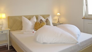 Una cama bien hecha con ropa blanca y una variedad de almohadas, incluyendo una decorativa. Hay dos mesitas de noche con lámparas, una a cada lado de la cama.