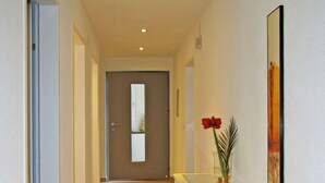Un pasillo con piso de madera, una consola blanca con un jarrón de flores rojas y un cuadro en la pared.