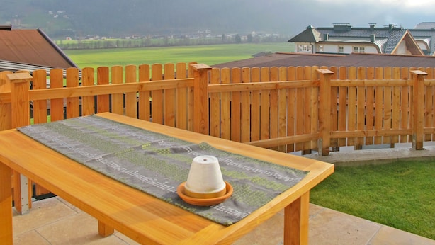 Una terraza de madera con una mesa y un objeto cónico, con vistas a un campo verde y casas.