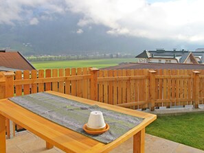 Een houten terras met een tafel en een kegelvormig voorwerp, met uitzicht op een groen veld en huizen.