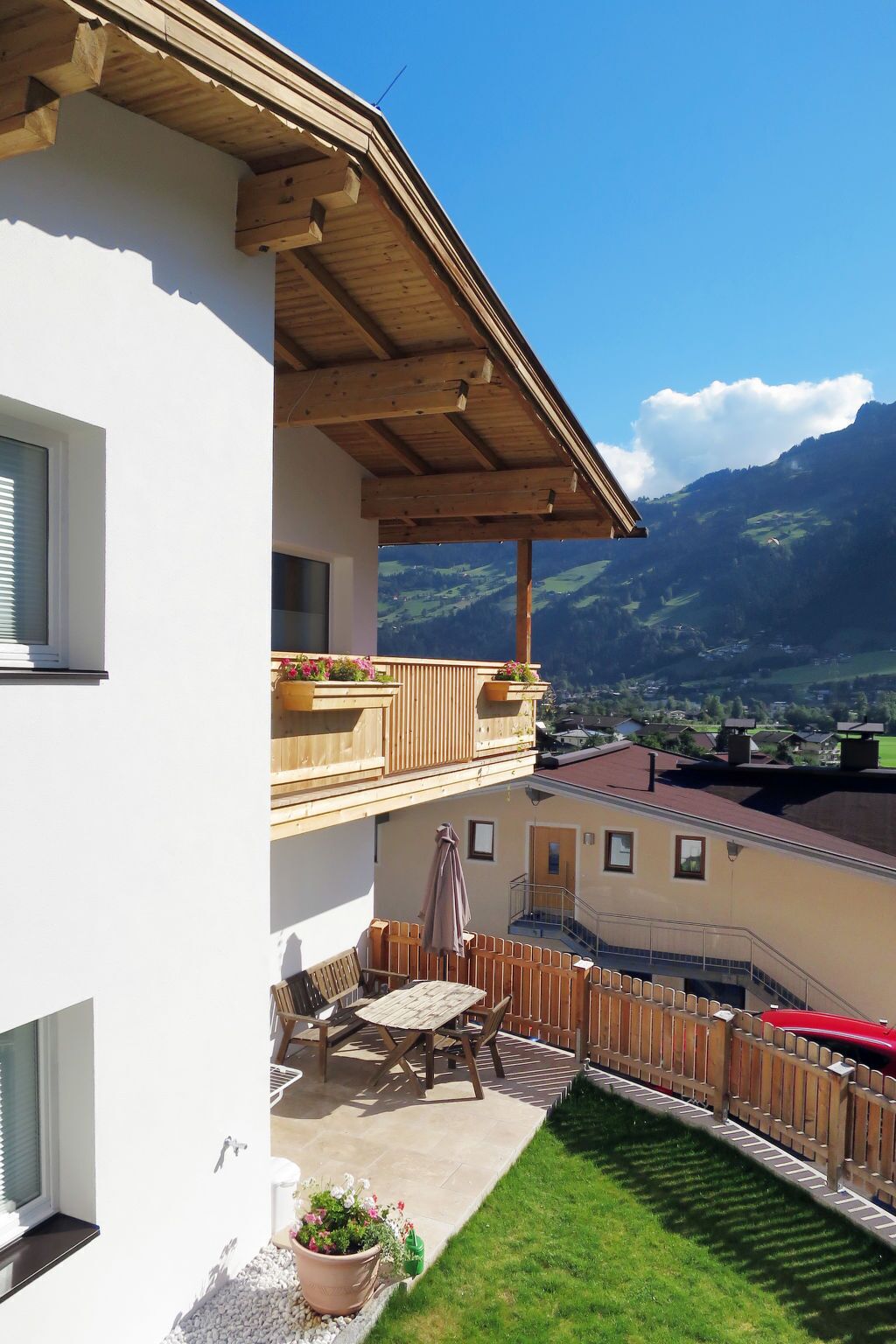 A two-story building with a wooden balcony, outdoor seating, and a view of mountains.
