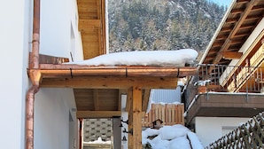 Una escalera conduce a un edificio de madera con tejado nevado y una vista de montaña al fondo.