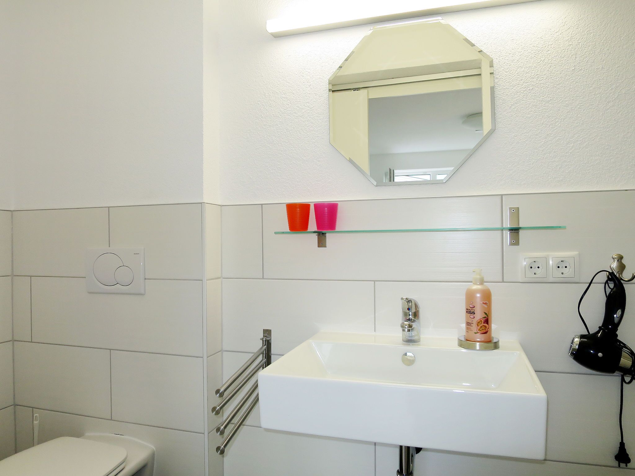 A bathroom with a white sink, a mirror, and a glass shelf with two pink cups.