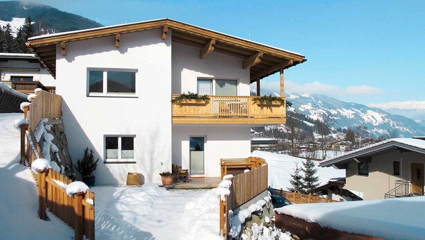 Un chalet de dos pisos con balcón, rodeado de nieve y montañas al fondo.