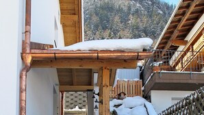 Una escalera conduce a un edificio de madera con tejado nevado y una vista de montaña al fondo.