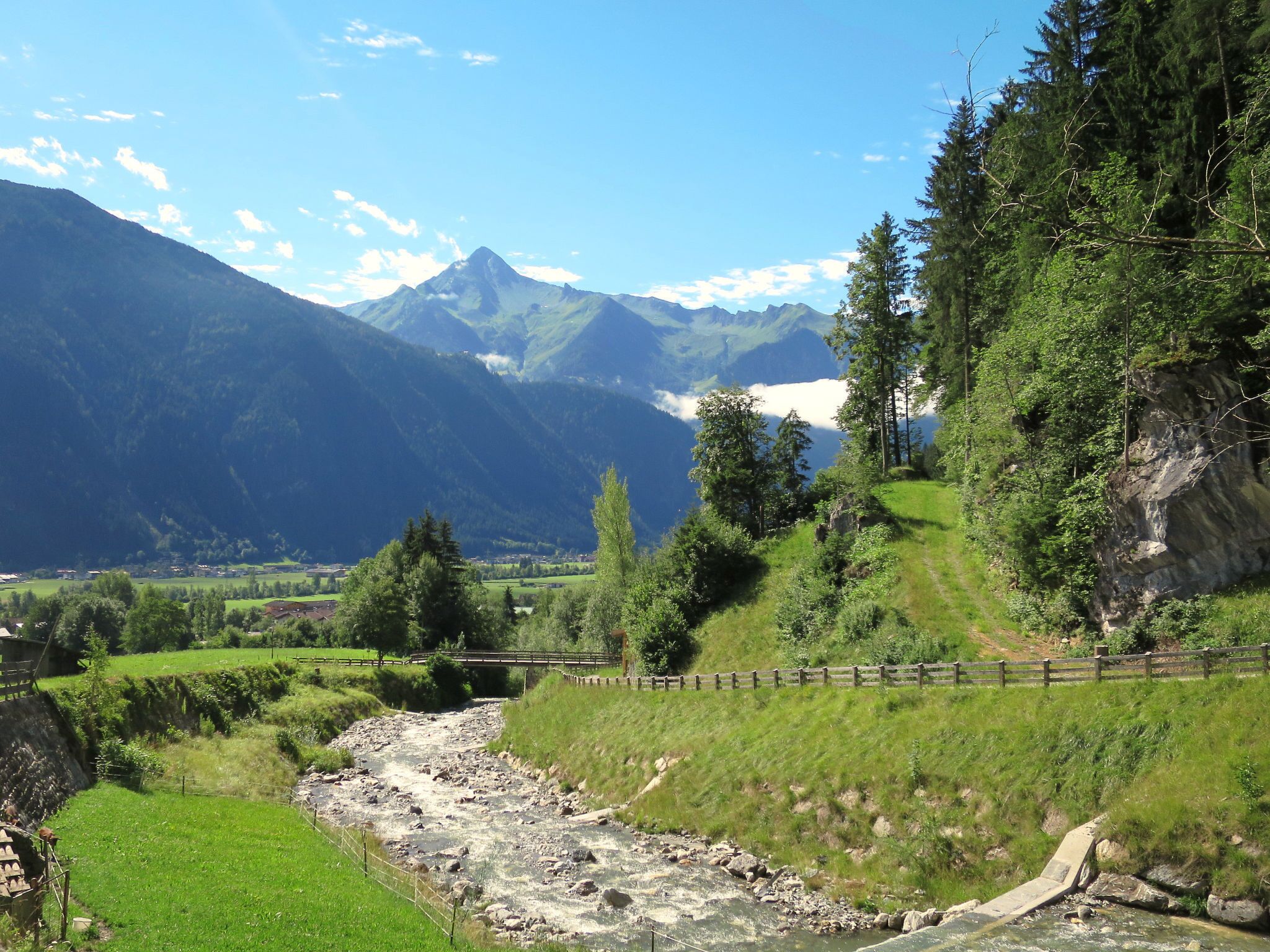 Un paysage montagneux avec une rivière, un pont en bois et une zone boisée.