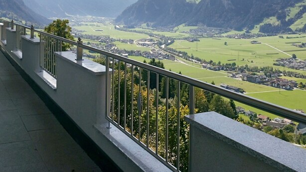 Un balcon doté d’une balustrade en métal, donnant sur une vallée avec des montagnes en arrière-plan.