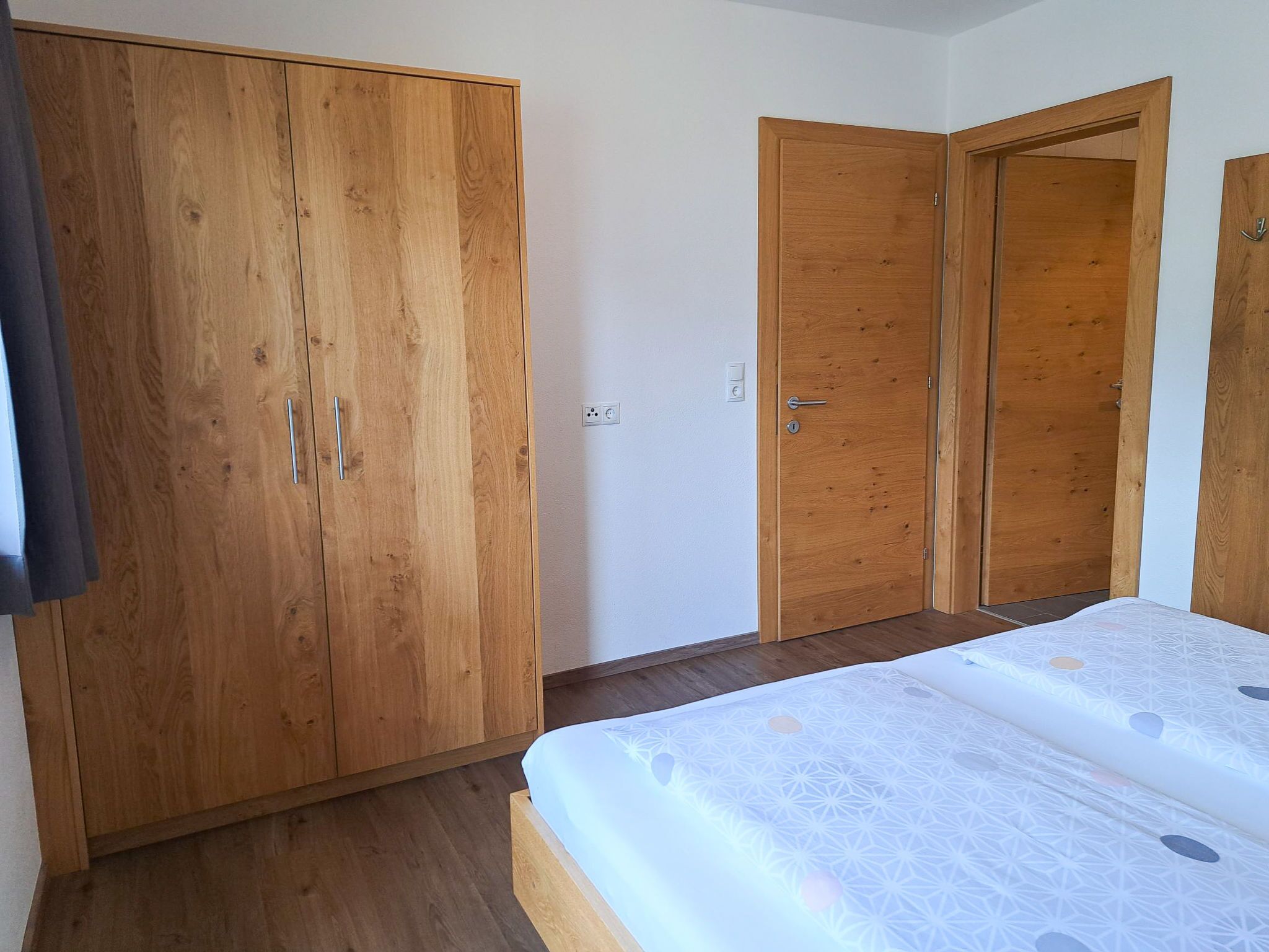A bedroom with a wooden wardrobe, a door, and a bed with a patterned bedspread.