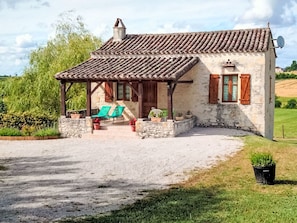 A rustic stone house with a tiled roof, a covered porch with two chairs, and a satellite dish.