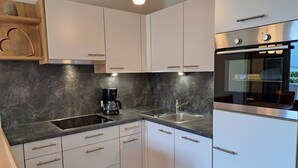 Cozinha moderna com armários brancos, bancada preta, cafeteira e forno embutido.