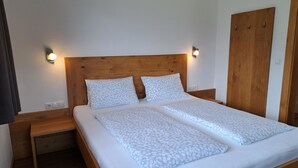 Uma cama de casal com cabeceira de madeira, duas mesas de cabeceira e um guarda-roupa.