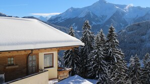 Un chalet in legno con tetto imbiancato dalla neve, un balcone e vista sulle montagne innevate.